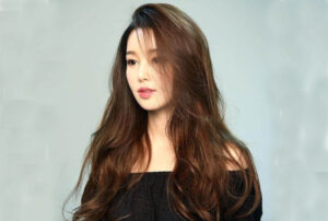 Kiểu tóc dài gợn sóng kết hợp mái rẽ ngôi lệch rất phù hợp cho mặt tròn trán cao.