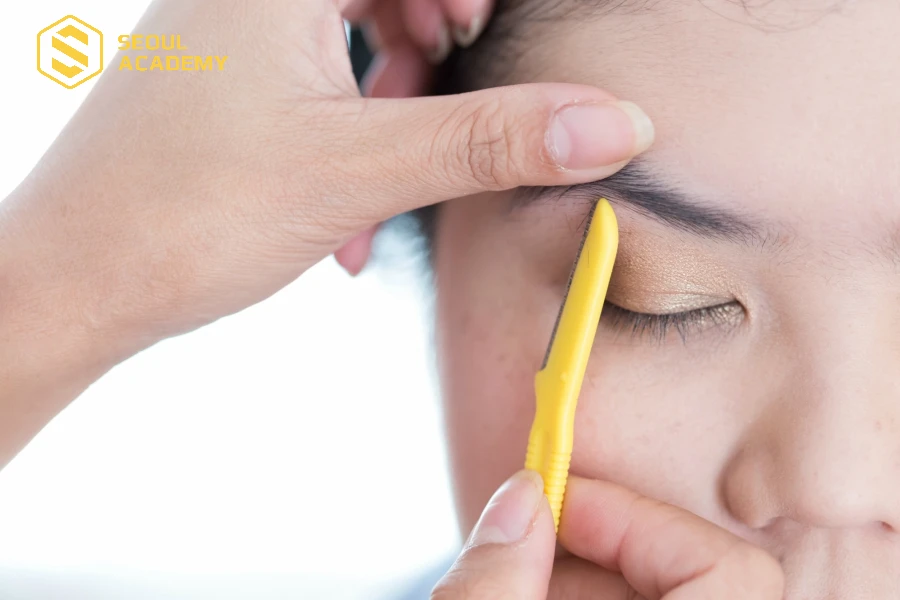 Dùng nhíp nhổ hoặc dao cạo để tỉa gọn chân mày để thực hiện vẽ chân mày bằng bút chì dễ dàng hơn