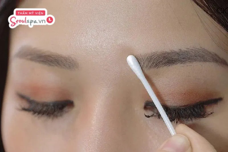 Vệ sinh chân mày bằng tăm bông thấm nước muối sinh lý để làm sạch bụi bẩn, mồ hôi và ngăn ngừa nguy cơ viêm nhiễm
